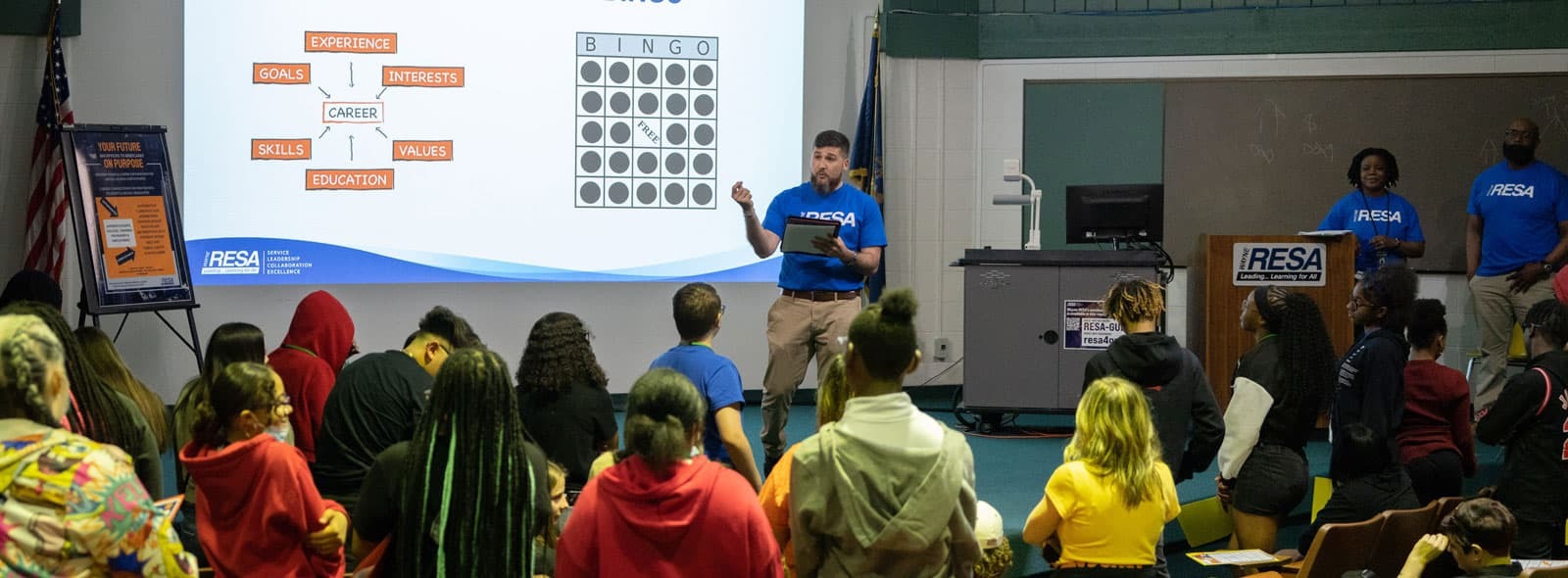 A team of individuals in blue shirts sits before a screen, focused on the content being displayed or discussed