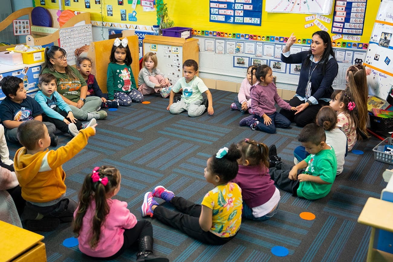 PreK students and teacher sitting in circle in classroom.